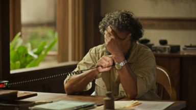 Marcos Palmeira como José Leôncio em cena de Pantanal; ele está sentado, com a mão escondendo o rosto e segura um rádio transmissor na mão 