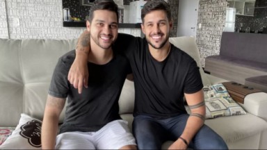 Diogo Mussi e Rodrigo Mussi  abraçados e sorridentes sentados em um sofá 