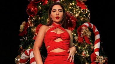 Jade Picon, de vestido vermelho, com uma árvore de Natal ao fundo 