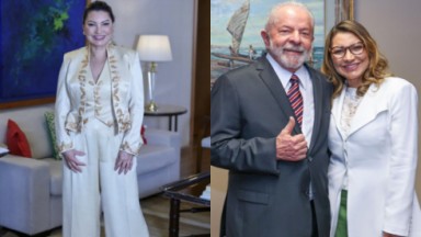 Janja sorridente com o look que usou na posse e ao lado de Lula, que usa terno e gravata e ela uma blazer branco e óculos de grau 
