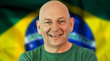 Luciano Hang posa para foto sorrindo com a bandeira do Brasil ao fundo. 