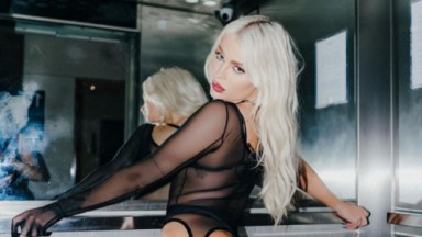 Luísa Sonza de roupa preta transparente fazendo pose em elevador, com os cabelos soltos e os braços abertos 