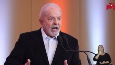 Lula falando em microfone com camisa branca e paletó preto; expressão brava 