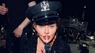 Madonna de trança, com chapéu preto e dedo na boca 