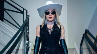 Madonna de óculos escuros e roupa preta, de chapéu branco, em escada, sem sorrir 