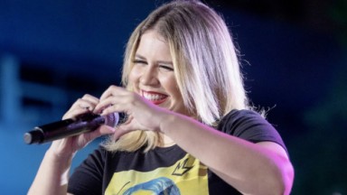 Marília Mendonça em show segurando microfone e fazendo gesto de coração 