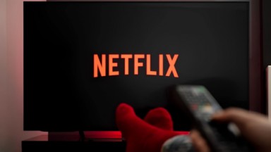 Arte com o logo da Netflix e uma pessoa de meias e com controle remoto na mão 