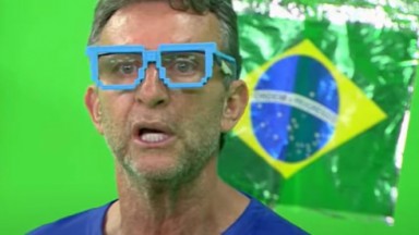 Neto com óculos azul e bandeira do Brasil ao fundo 