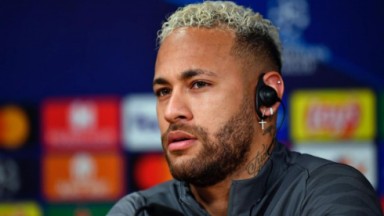 Neymar com fone no ouvido e casaco preto olhando para a frente com expressão séria 
