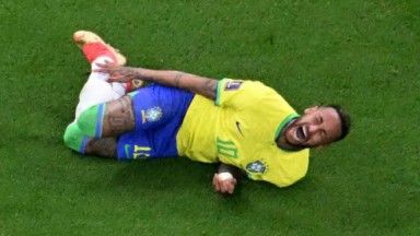 Neymar gritando de dor, deitado na grama, com a mão no tornozelo 
