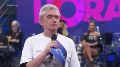 Serginho Groisman no Altas Horas, segurando microfone e ficha, de camiseta branca 