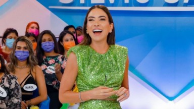 Patrícia Abravanel sorrindo, de vestido verde, no cenário do Programa Silvio Santos 