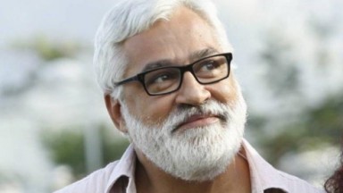 De óculos, o autor de novelas Paulo Halm olha para cima, em pose reflexiva 