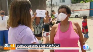 Mulher levantando placa de "Fora Jade" enquanto repórter entrevista moradora 