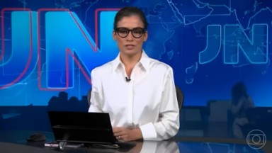 Renata Vasconcellos de camisa branca e cabelo preso na bancada do Jornal Nacional 