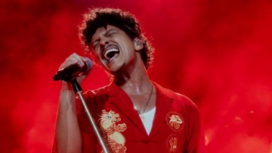 Bruno Mars de roupa vermelha, cantando e segurando microfone 