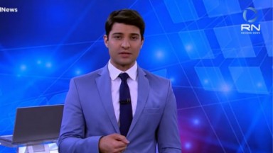 Rafael Algarte de terno e gravata azuis e camisa branca no cenário do News 19 Horas, da Record News 