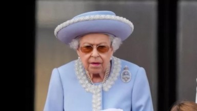 Rainha Elizabeth II, de chapéu azul, óculos escuros e brinco de pérola 