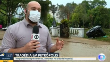 Repórter em Petrópolis com microfone da Globo e camisa clara 