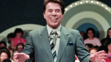 Silvio Santos de terno cinza e gravata listrada, na frente de auditório 