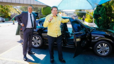 Silvio Santos de camisa amarela saindo do carro  