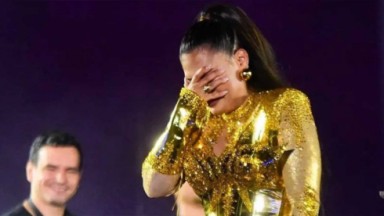 Simone Mendes chorando no palco, com a mão no rosto 