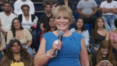 Susana Vieira sorrindo, de roupa azul, segurando microfone 
