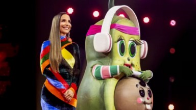 Ivete Sangalo com a Mamãe Abacate no palco do The Masked Singer Brasil, a apresentadora sorrindo de vestido colorido e cabelo solto 
