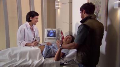 Cena de Ti Ti Ti com Marcela deitada numa maca, uma médica ao lado fazendo ultrassom e Edgar de mãos dadas com ela 