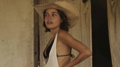 A atriz Julia Dalavia, como Guta, usando um biquíni e chapéu em cena de Pantanal 