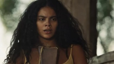A atriz Bella Campos, como a personagem Muda, com cabelos soltos e vestido amarelo em cena de Pantanal 