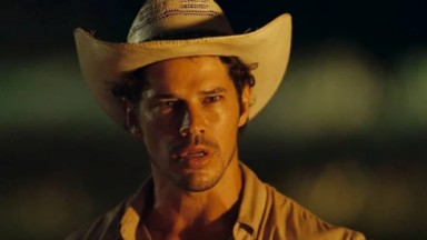 Jose Loreto, como Tadeu, de boca aberta e usando chapeú em cena de Pantanal 