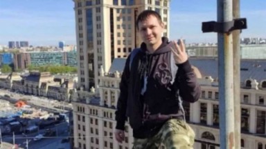 Dima Vert em cima de prédio, posado, mostrando três dedos 