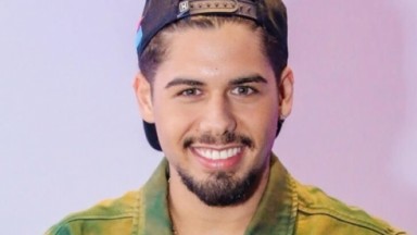 Zé Felipe sorrindo para foto com boné e jaqueta tie-dye 