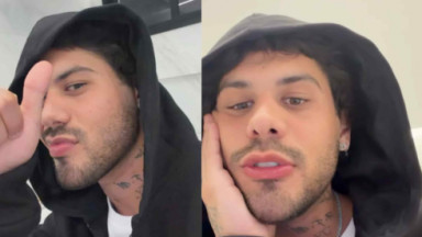 Zé Felipe de capuz preto com mão no queixo e fazendo joinha 