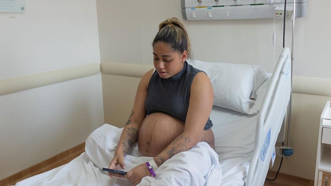 MC Loma grávida, sentada em cama de hospital mexendo no celular