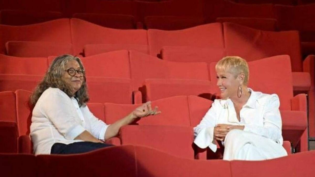 Marlene Mattos e Xuxa Meneghel conversando em poltronas vermelhas