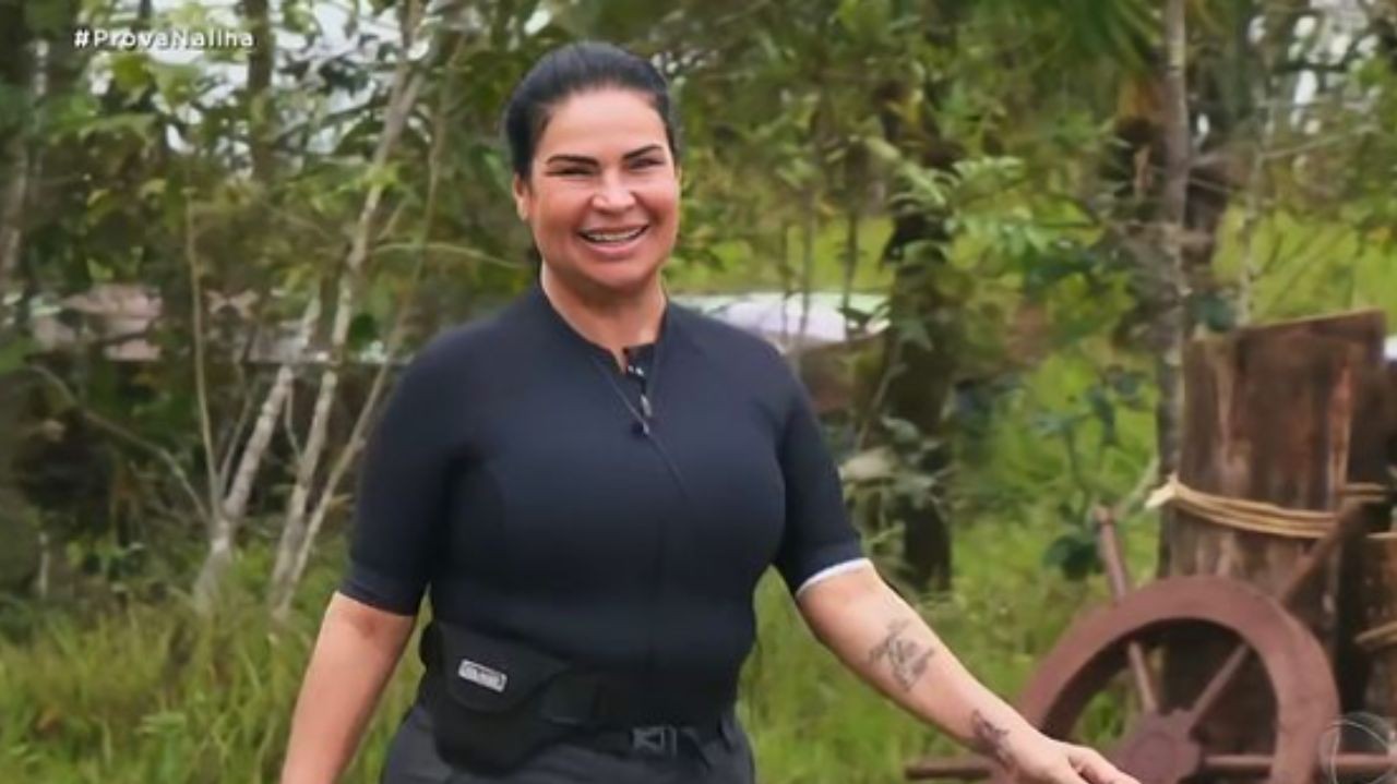 Solange Gomes de roupa preta andando e sorrindo no cenário do Ilha Record