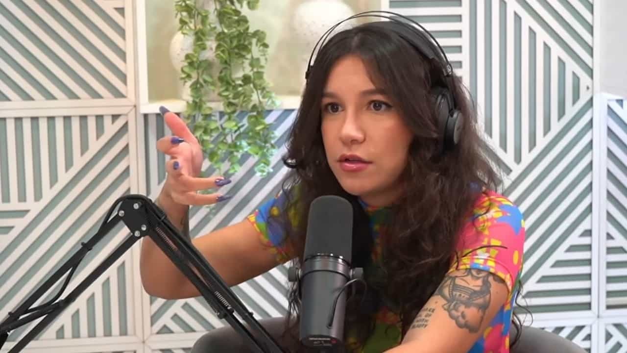 Priscilla Alcântara de blusa colorida e fones de ouvido, falando perto de microfone