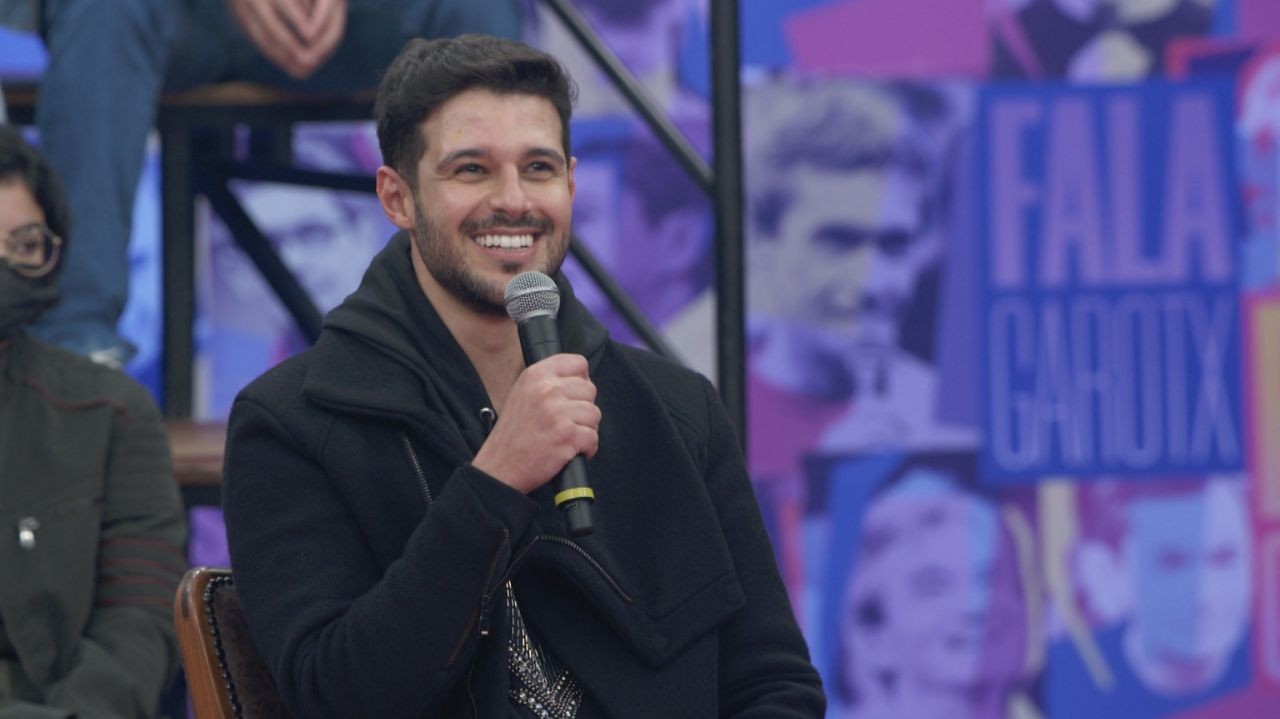 Rodrigo Mussi de roupa escura, sorrindo e segurando microfone