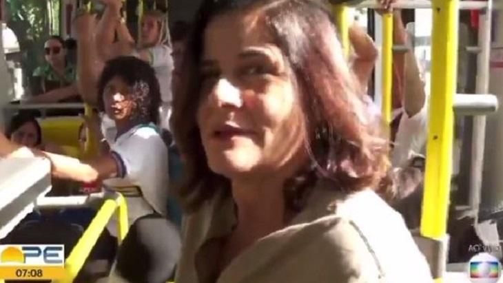 Repórter da Globo dentro de um ônibus, de pé. 