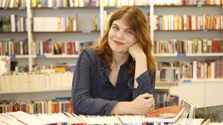 Cláudia Lage sentada em uma biblioteca, rodeada de livros.
