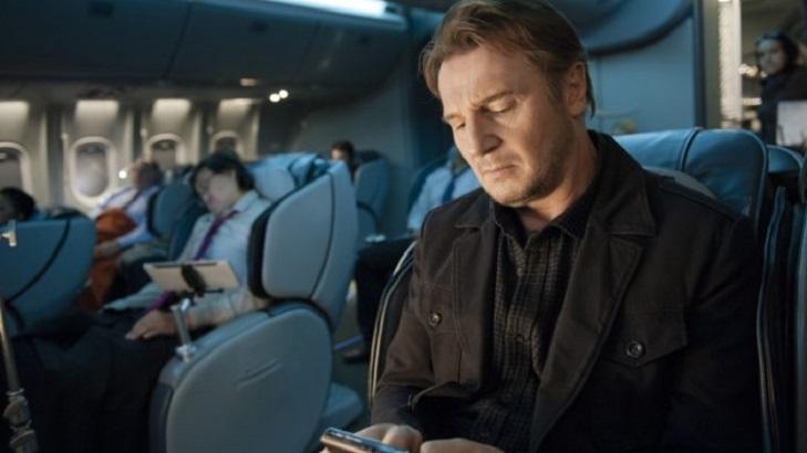 Cena do filme Sem Escala em que o protagonista está sentado na poltrona de um avião enquanto olha no celular.