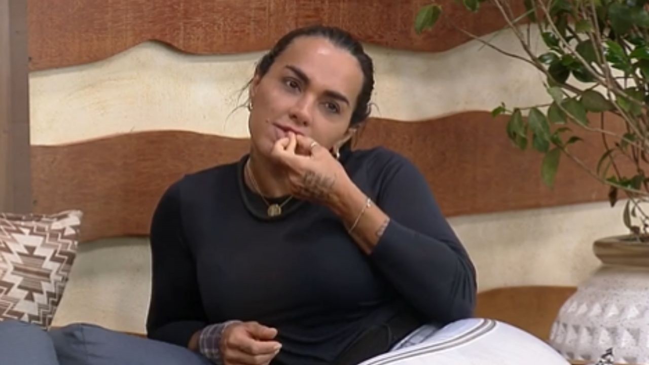 Kamila Simioni de calça cinza e blusa de frio preta, com cabelo preso e mão na boca