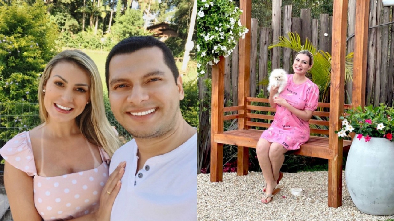 Andressa Urach sorridente ao lado do marido e sentada em um banco de madeira, com um vestido rosa, segurando um cachorrinho no colo.
