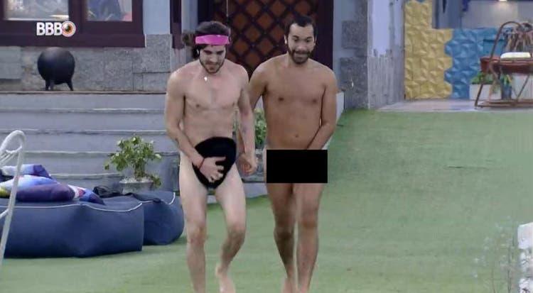 Fiuk e Gilberto estão pelados escondendo as partes íntimas com a mão e um chapéu caminhando até a piscina do BBB21
