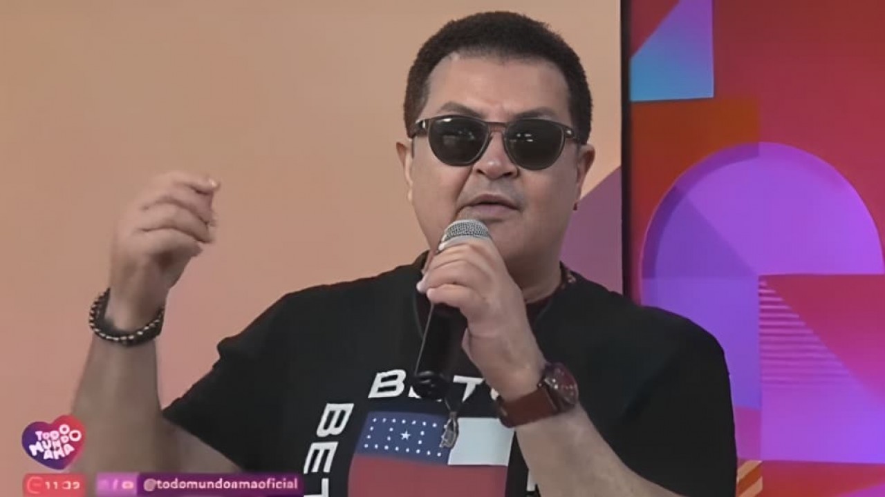 Beto Barbosa de camiseta preta e óculos escuros, falando em microfone