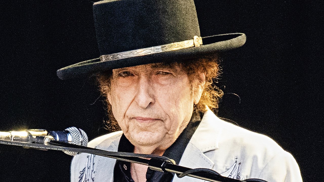 Bob Dylan de chapéu diante de microfone