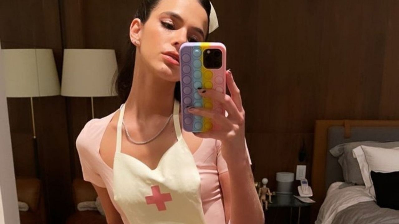 Bruna Marquezine com vestido rosa e apetrechos de enfermeira posando em frente ao espelho com o celular na mão
