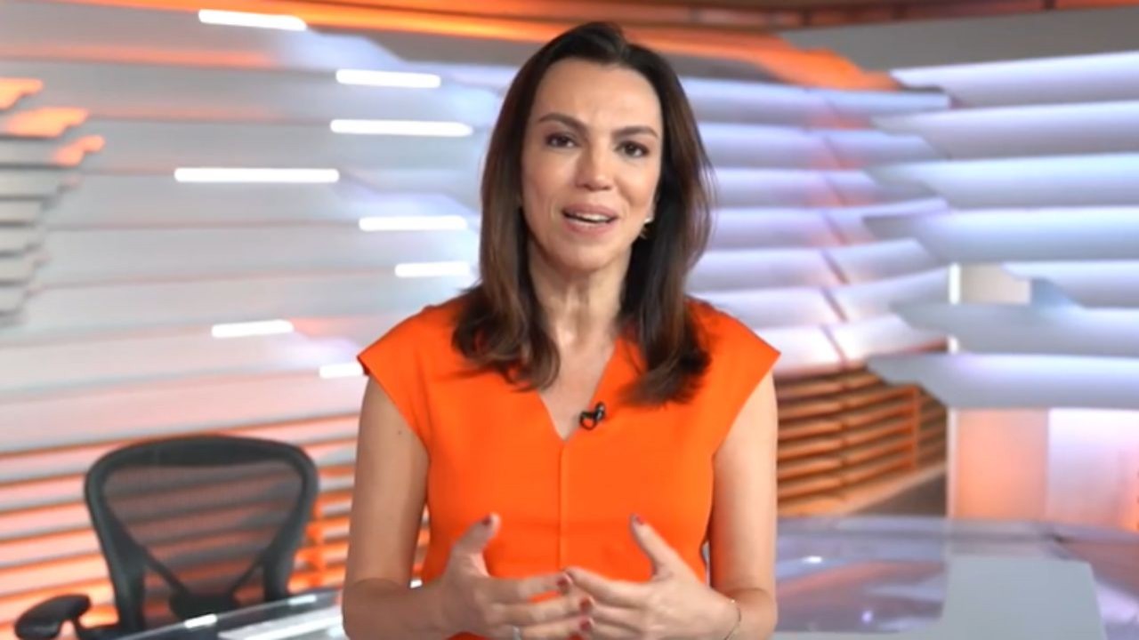 Ana Paula Araujo falando e gesticulando, de roupa laranja, no estúdio do Bom Dia Brasil